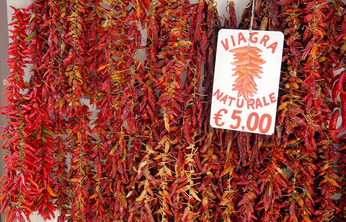 Red chili peppers hanging with a handwritten sign reading “Viagra Naturale €5”