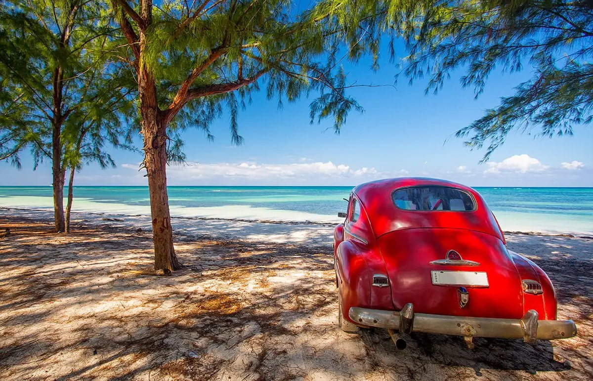 Classic vintage red car on a tropical beach in Cuba, Caribbean luxury yacht charter destination