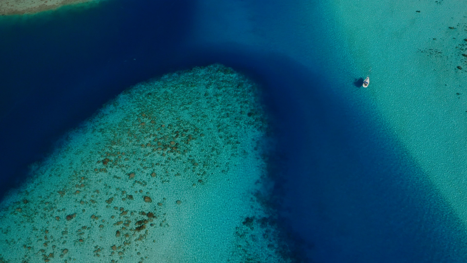 Aerial view of turquoise waters and coral reefs in the British Virgin Islands with a yacht at anchor