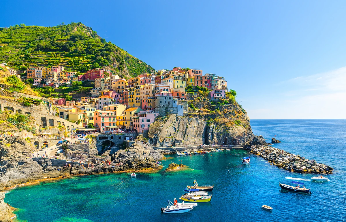 Manarola traditional typical Italian village in National park Cinque Terre, colorful multicolored buildings houses on rock cliff, fishing boats on water, blue sky background, La Spezia, Liguria, Italy