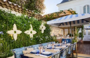Al fresco dining setup with a long table, blue and white tableware, and a vine-covered wall with white floral shapes.